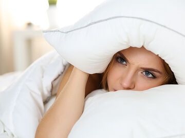 Frau leidet unter Schlafstörung und versteckt ihren Kopf in einem Kopfkissen während des Schlafens