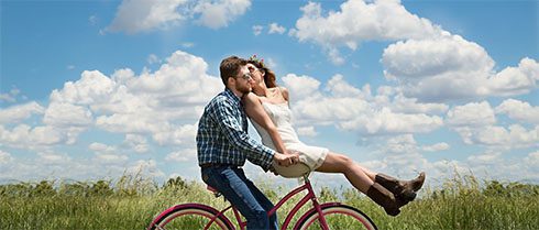 Ein verliebtes Paar auf einem Fahrrad vor Schäfchenwolken